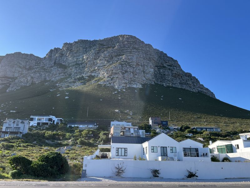 A scenic view of a residential hillside property set against a prominent mountain backdrop under a clear blue sky.