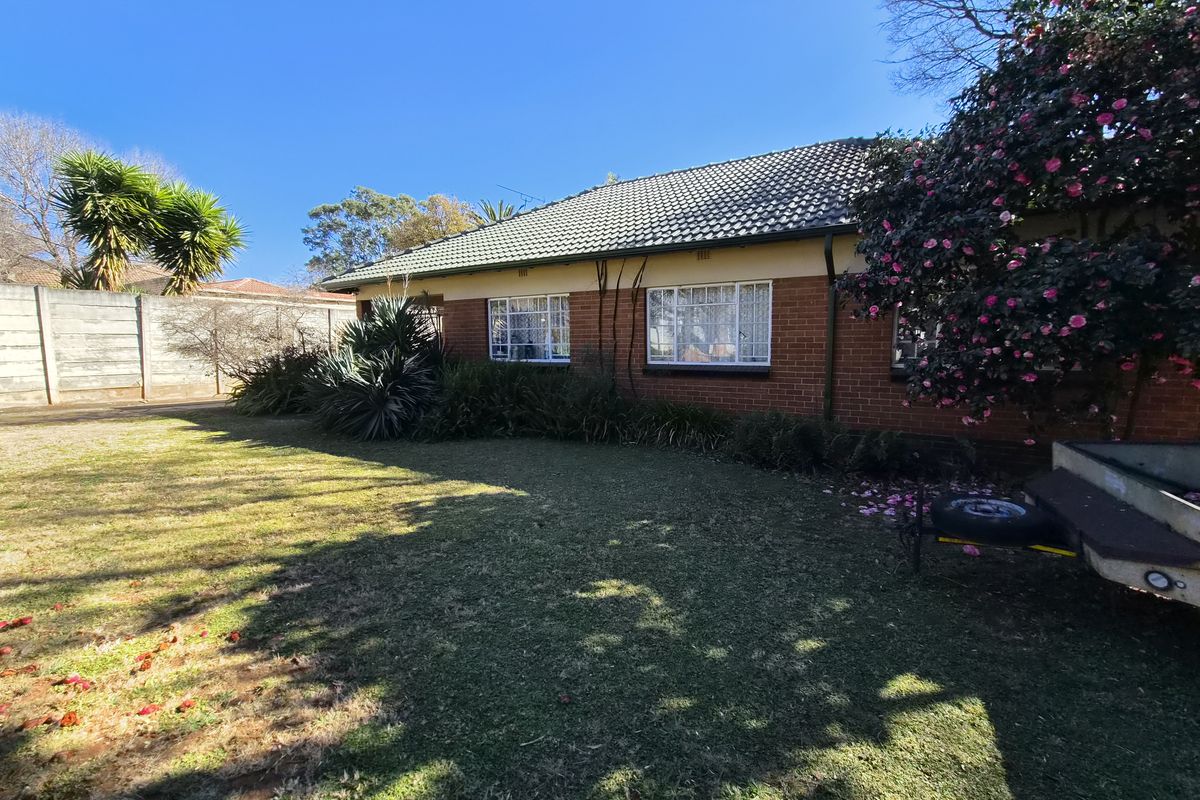 A view of the rear brick facade of the house, featuring a tiled roof, steel-framed windows, and a spacious garden with a boundary wall.