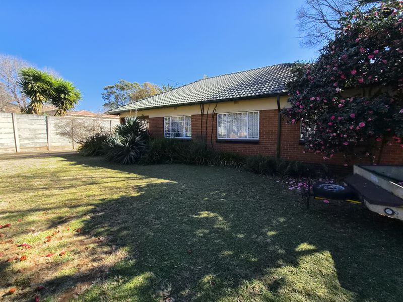 A view of the rear brick facade of the house, featuring a tiled roof, steel-framed windows, and a spacious garden with a boundary wall.