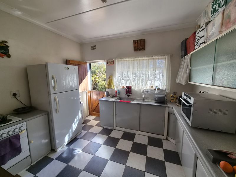 A functional kitchen featuring checkerboard floor tiles, built-in cabinetry, a stainless steel sink, and a stable door providing direct access to the exterior.