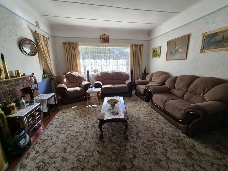 A traditional living room featuring a brick fireplace, coved ceilings, and large windows, offering a classic layout with potential for modern updates.