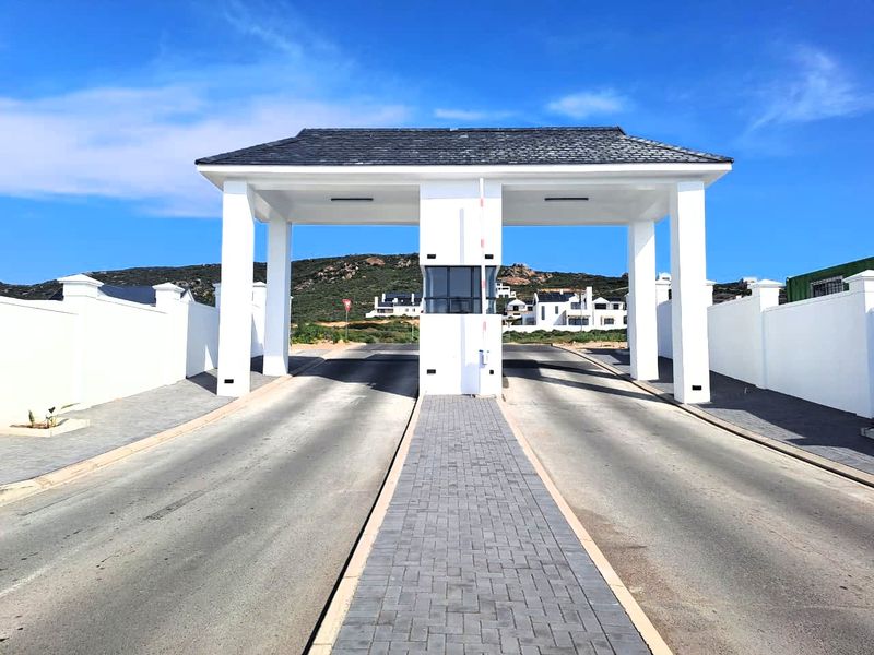 A well-maintained residential estate entrance featuring a modern security gatehouse, paved dual-lane driveway, and perimeter walling.