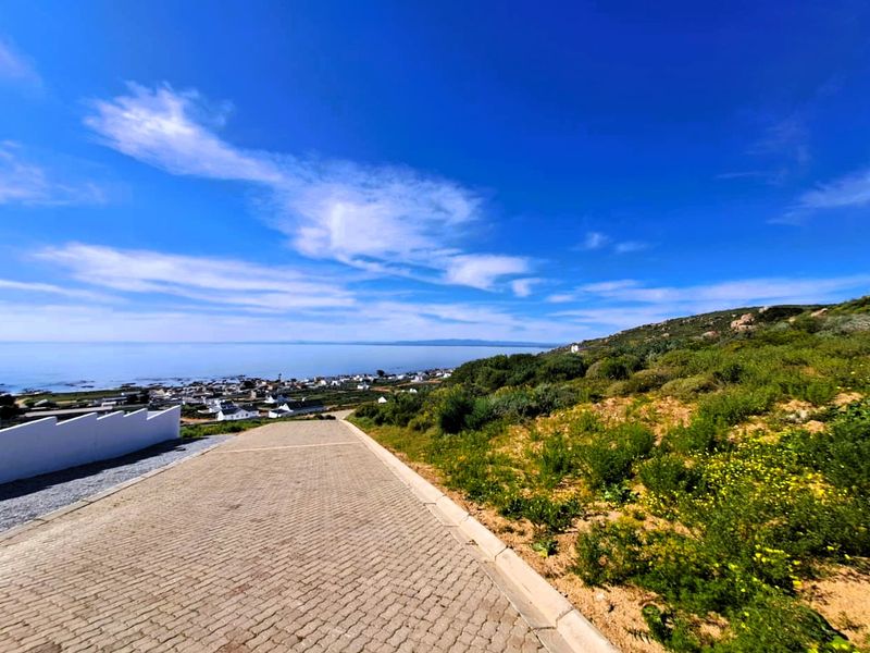 A scenic view overlooking the coastal landscape and residential area, featuring a paved driveway leading down towards the horizon.