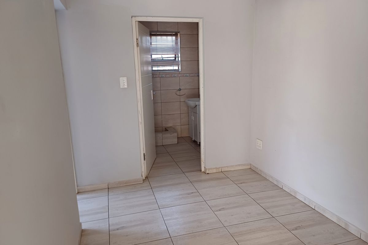 An empty bedroom featuring neutral tiled flooring and a doorway leading to an en-suite bathroom with tiled walls.