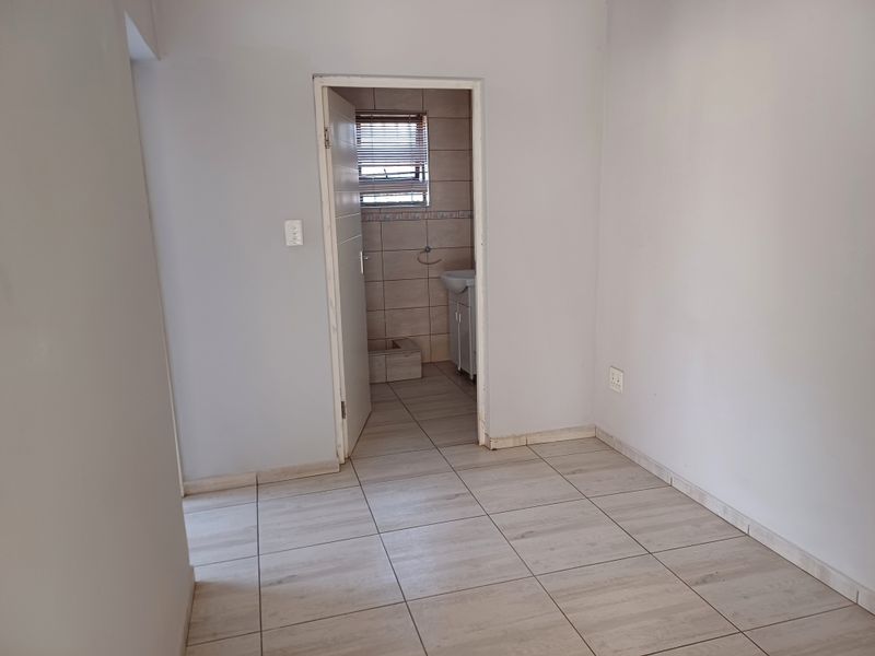 An empty bedroom featuring neutral tiled flooring and a doorway leading to an en-suite bathroom with tiled walls.