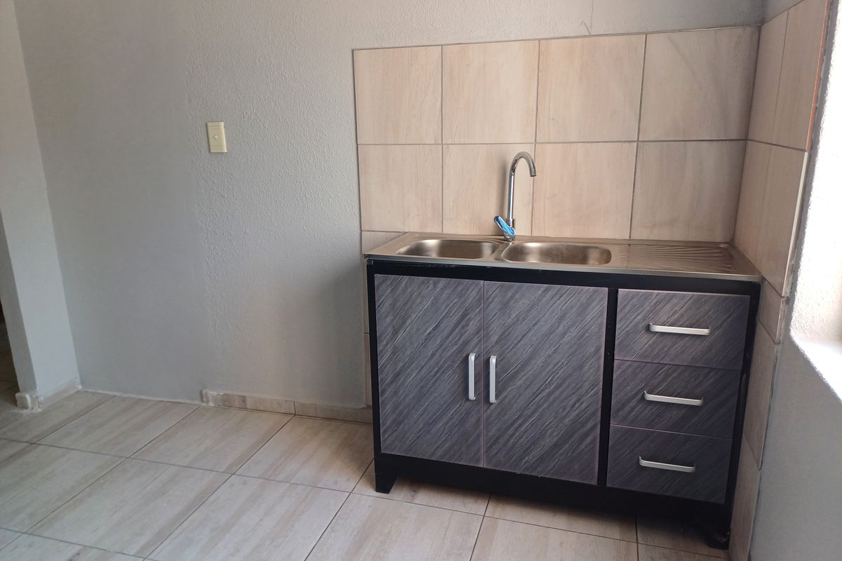 A compact kitchen area featuring a stainless steel sink, built-in cabinetry, and tiled splashback in a neutral, functional space.