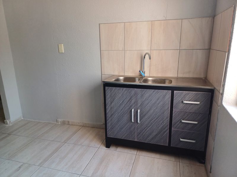 A compact kitchen area featuring a stainless steel sink, built-in cabinetry, and tiled splashback in a neutral, functional space.