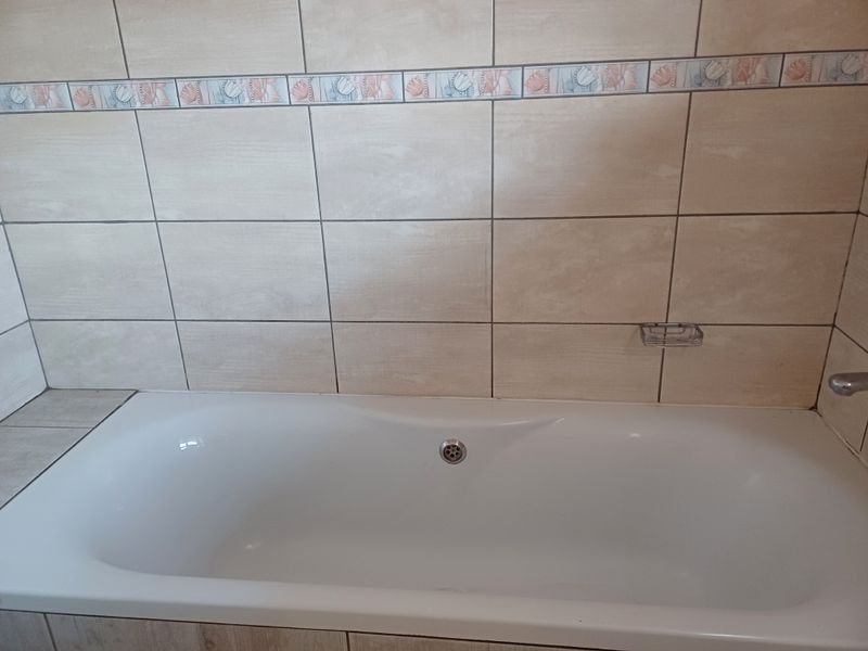 A clean bathroom featuring a built-in bathtub with neutral ceramic wall tiles and a decorative accent border.