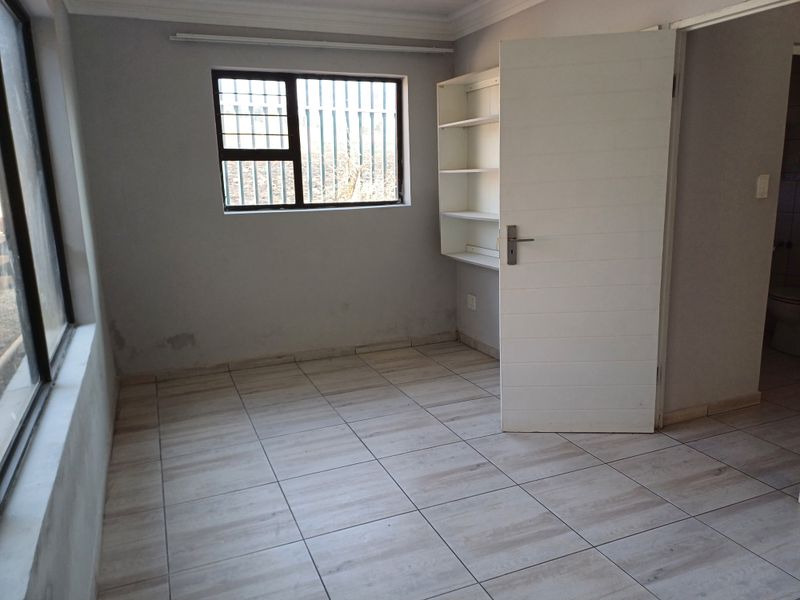 An empty bedroom featuring tiled flooring, built-in shelving, and a window with security bars, requiring minor cosmetic updates to the walls.