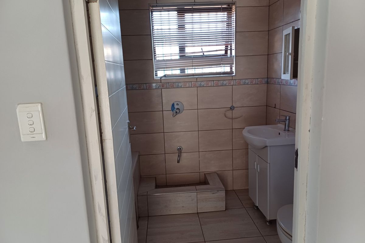 A compact bathroom featuring tiled walls and flooring, a vanity basin, toilet, and a shower area currently missing a shower head.