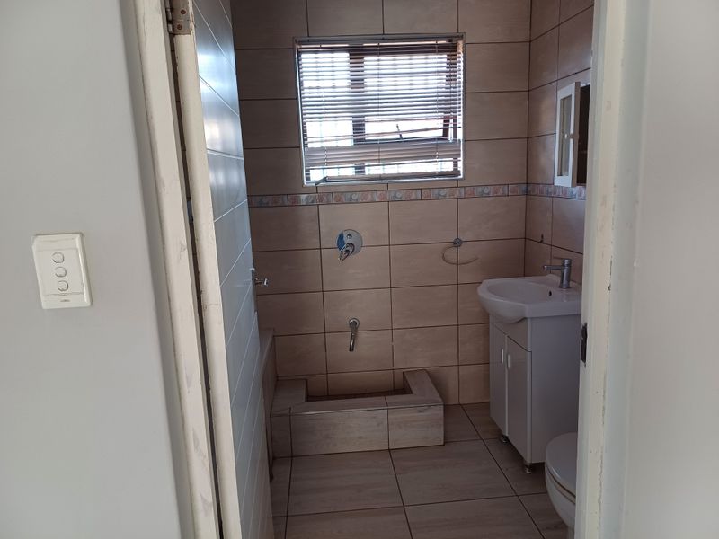 A compact bathroom featuring tiled walls and flooring, a vanity basin, toilet, and a shower area currently missing a shower head.
