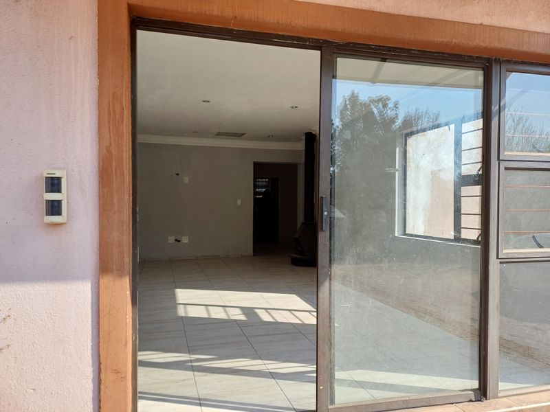 An empty, open-plan living area featuring tiled floors, a freestanding fireplace, and large sliding glass doors providing access to the exterior.