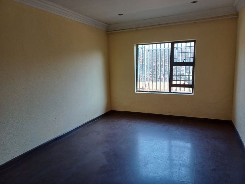 An empty bedroom featuring dark laminate flooring, yellow walls with cornice detailing, and a window fitted with security bars.