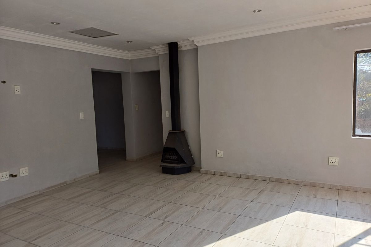 Spacious, empty living area featuring neutral tiled flooring, recessed lighting, and a modern freestanding fireplace, offering a clean and versatile blank canvas.
