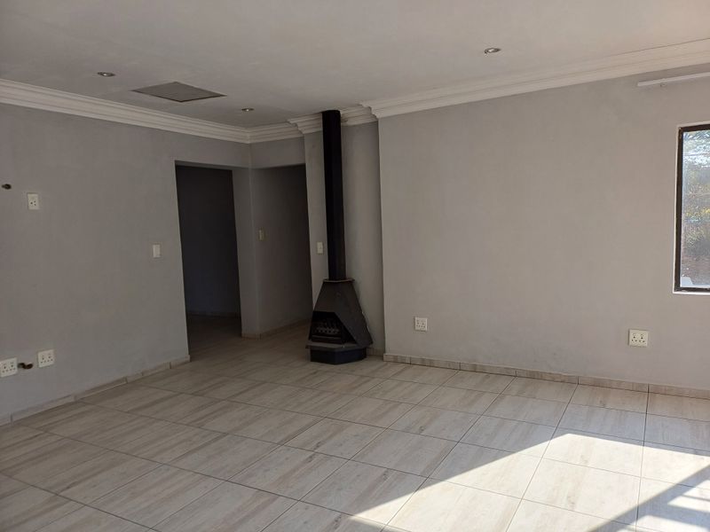 Spacious, empty living area featuring neutral tiled flooring, recessed lighting, and a modern freestanding fireplace, offering a clean and versatile blank canvas.