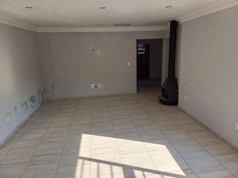 An empty living room featuring tiled flooring, a freestanding fireplace, and recessed lighting, requiring minor wall repairs and cosmetic updates.