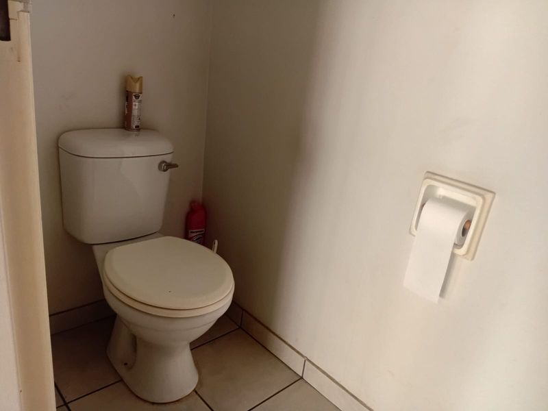 A compact bathroom featuring a standard toilet and wall-mounted toilet roll holder with tiled flooring.