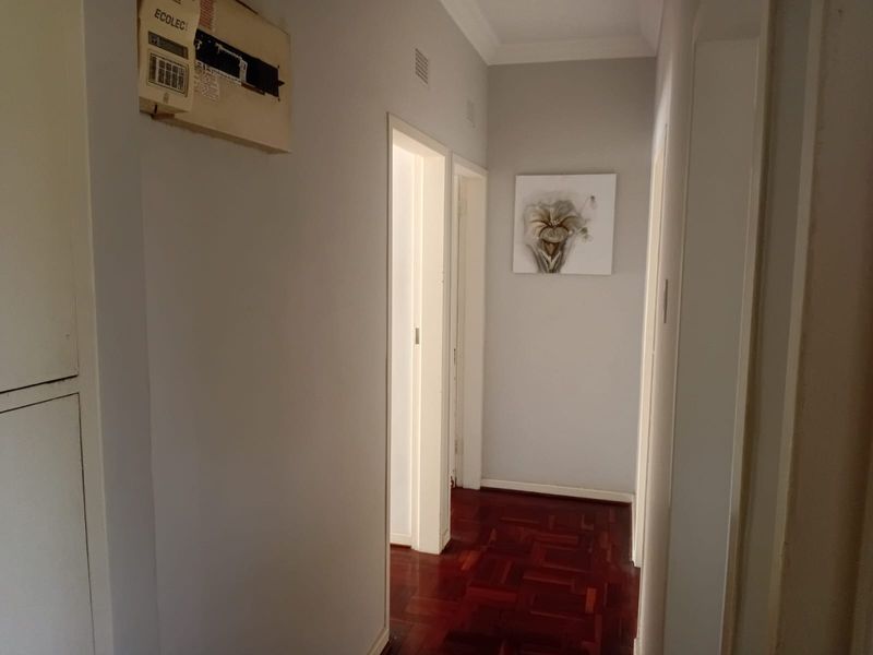 A clean, well-maintained hallway featuring polished parquet flooring, neutral wall finishes, and a wall-mounted electrical distribution board.