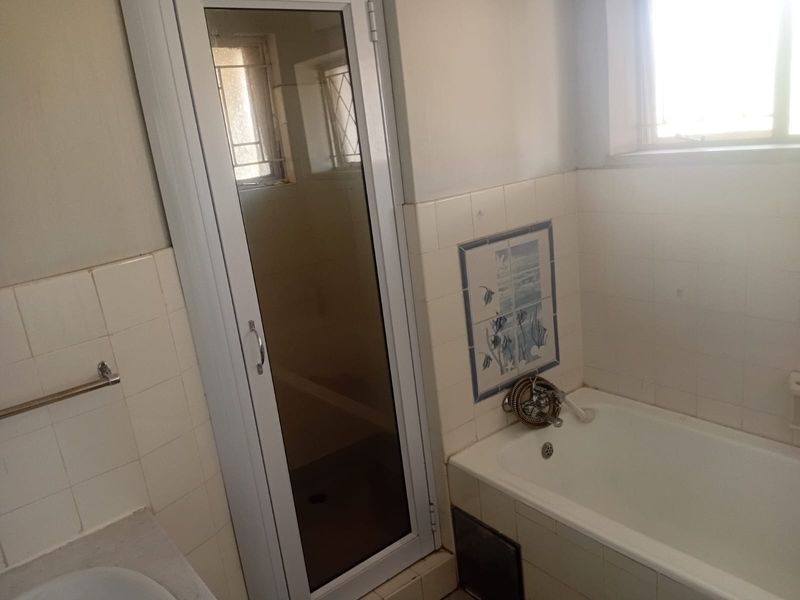 A dated bathroom featuring a bathtub, separate shower enclosure, and tiled walls, offering potential for a modern renovation.