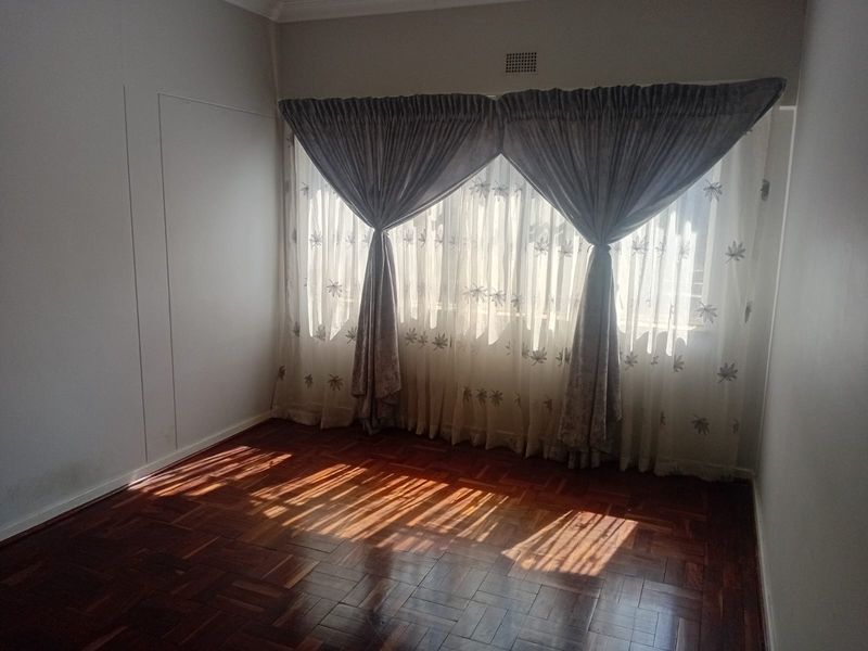 A bright, empty bedroom featuring classic parquet flooring and large windows with installed curtain tracks.