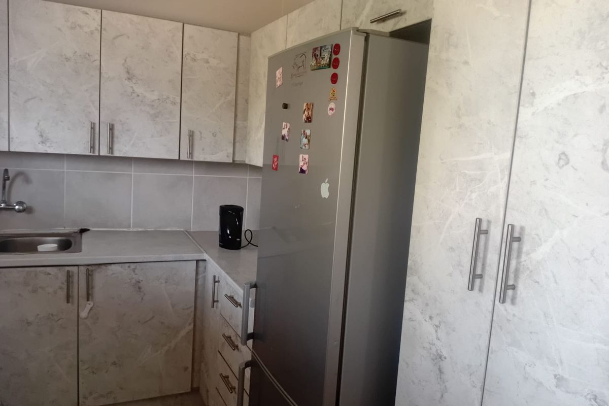 A functional kitchen featuring marble-effect cabinetry, a stainless steel sink, tiled backsplash, and ample built-in storage space.