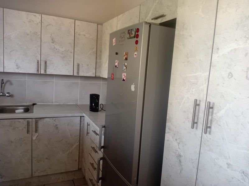 A functional kitchen featuring marble-effect cabinetry, a stainless steel sink, tiled backsplash, and ample built-in storage space.