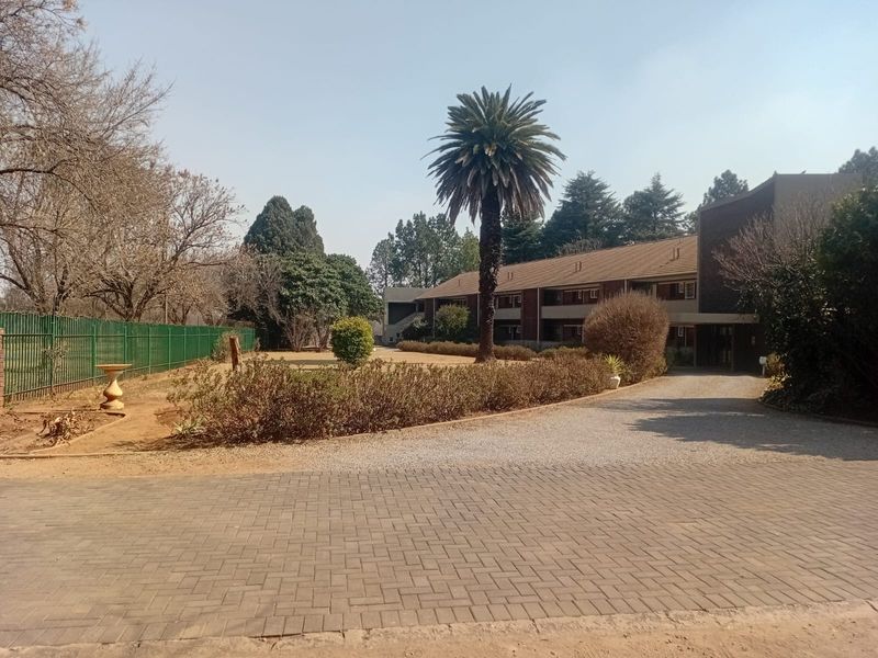 Exterior view of the apartment complex featuring a paved and gravel driveway, established garden, and perimeter fencing.