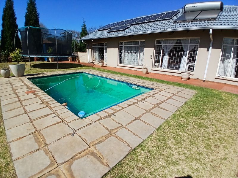 Rear exterior view featuring a swimming pool, paved surround, and a house roof equipped with solar panels and a solar water heating system.