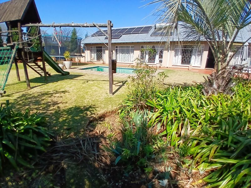 Rear view of the house featuring a swimming pool, landscaped garden, and solar panels installed on the tiled roof.