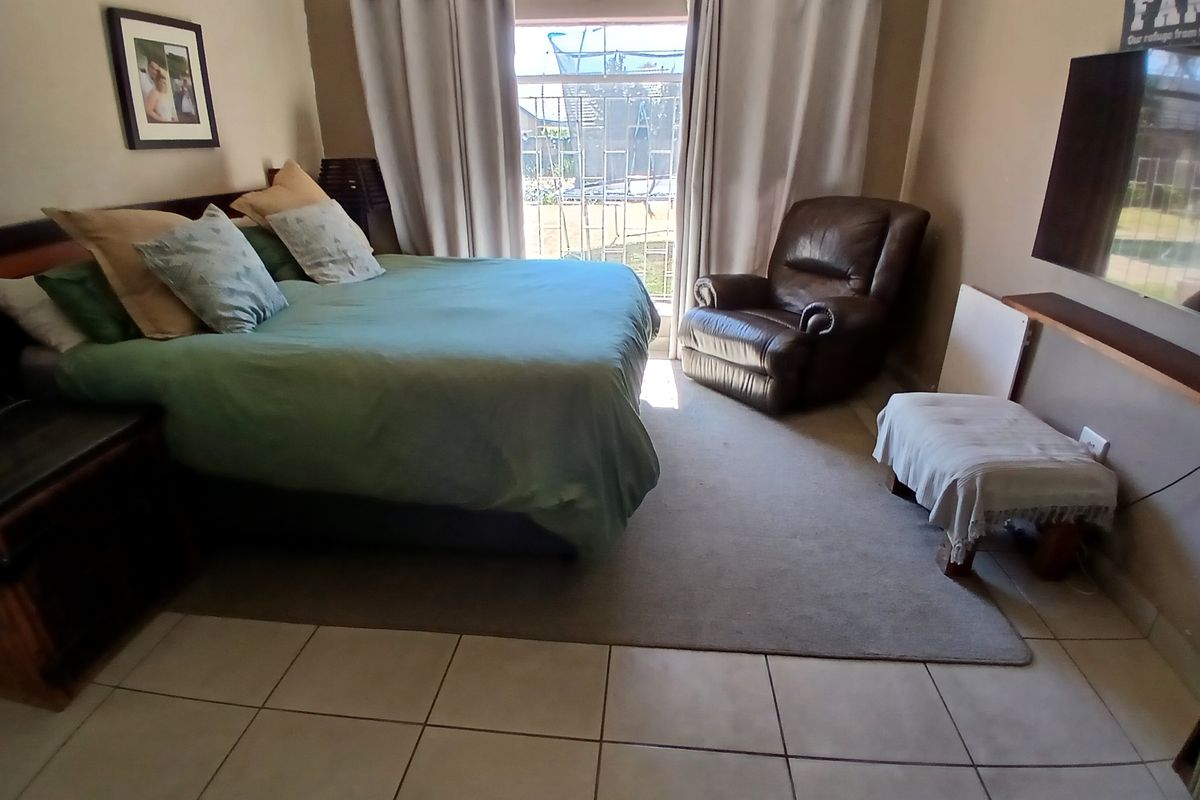 A bedroom featuring tiled flooring and a sliding glass door with security gate providing access to the exterior.