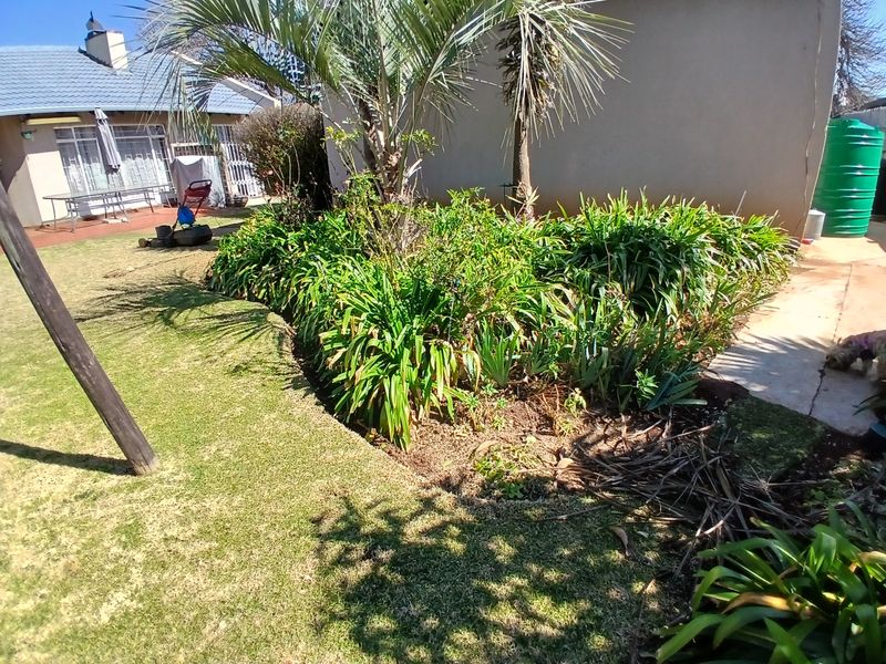 A residential backyard featuring a maintained lawn, established garden beds with mature plants, and a water storage tank.