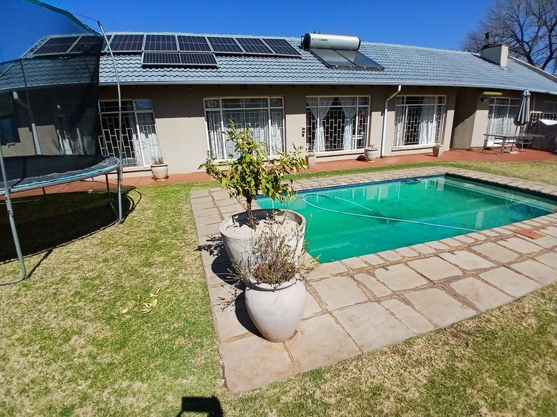 Rear exterior view of the house featuring a swimming pool, paved surround, and roof-mounted solar panels and water heating system.