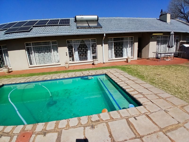 Rear exterior view featuring a swimming pool with paved surround, solar water heating system, and photovoltaic panels installed on the tiled roof.