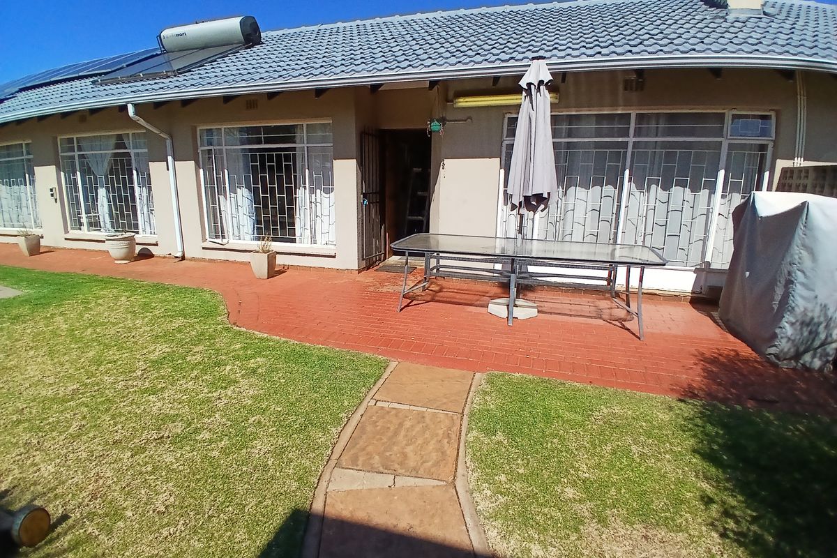 Rear view of the house featuring a brick paved patio, landscaped lawn, and a tiled roof equipped with a solar water heating system.