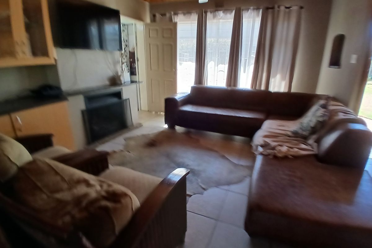 A living room featuring tiled flooring, a fireplace, and a timber ceiling with a ceiling fan, providing access to the outdoor area.