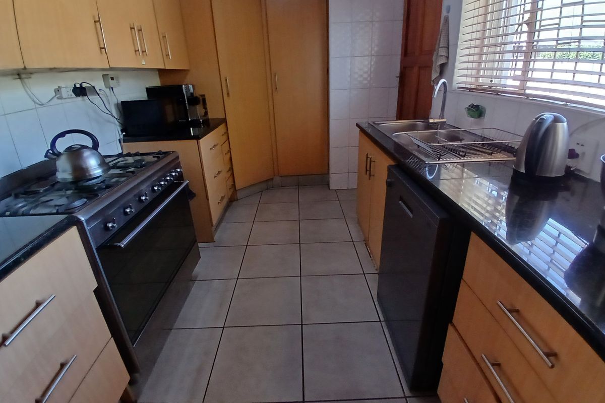 A functional kitchen featuring light wood cabinetry, dark granite countertops, a gas stove, and tiled flooring with a practical layout.