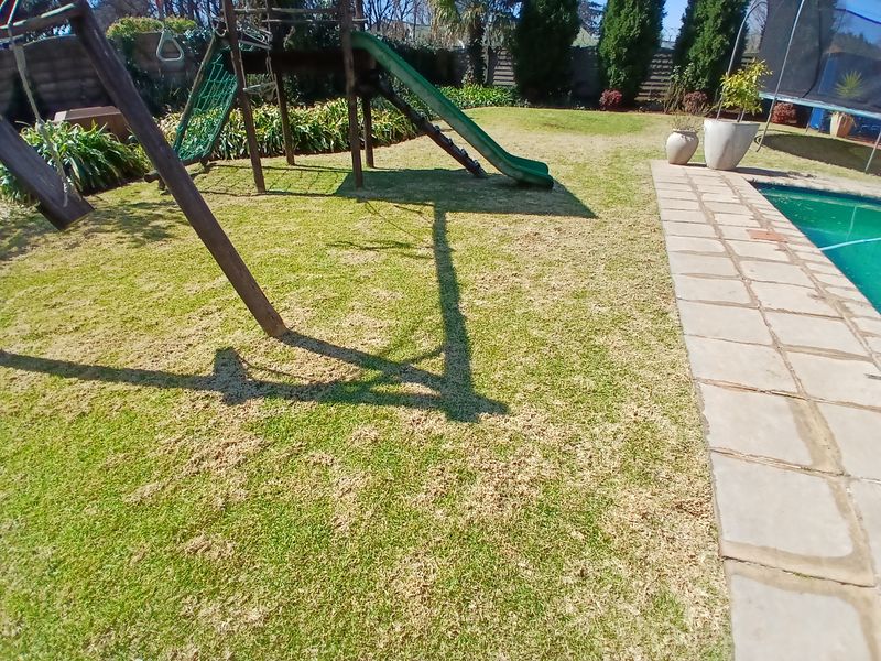 A backyard pool area featuring a paved surround, established lawn, and garden space.