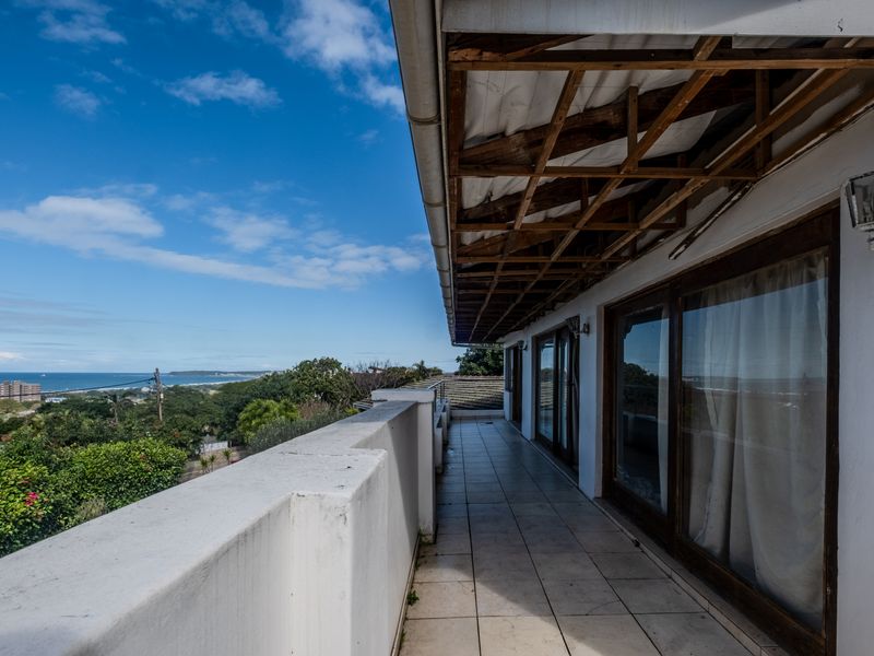 A spacious balcony featuring tiled flooring, a masonry balustrade, and an exposed timber roof structure, offering expansive coastal views.