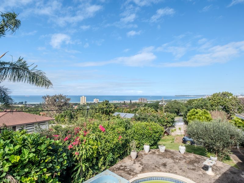 Elevated coastal view overlooking a lush garden, swimming pool, and the distant ocean horizon.