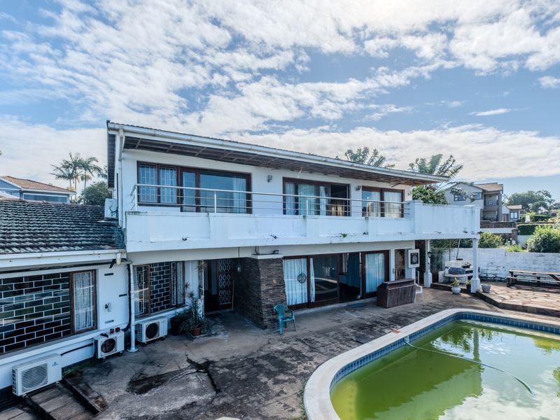 Rear view of a two-story house featuring a swimming pool, a large upper-level balcony, and sliding glass doors leading to the patio area.