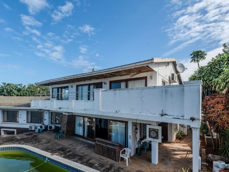 Rear view of a multi-level house featuring a balcony, sliding glass doors, and an outdoor swimming pool area requiring maintenance.