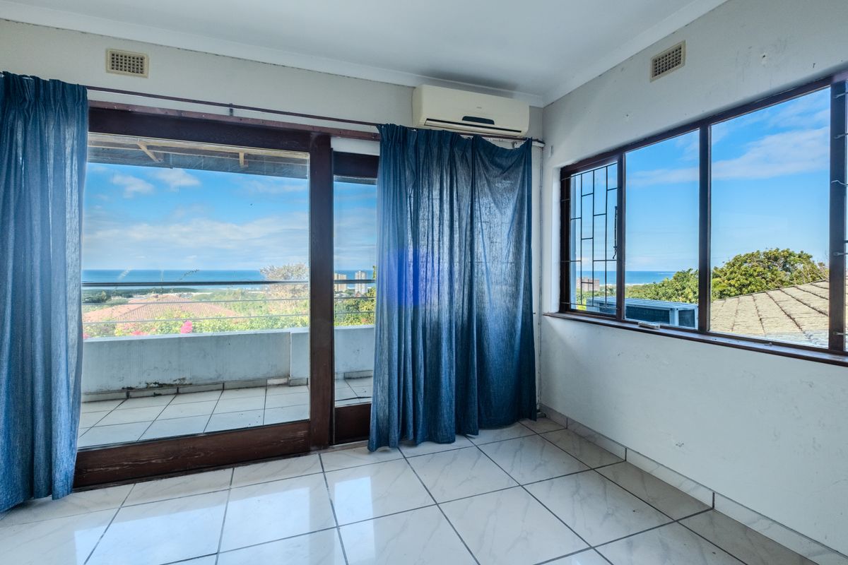 Bright living area featuring tiled floors, an air conditioning unit, and large sliding doors opening to a balcony with scenic ocean views.