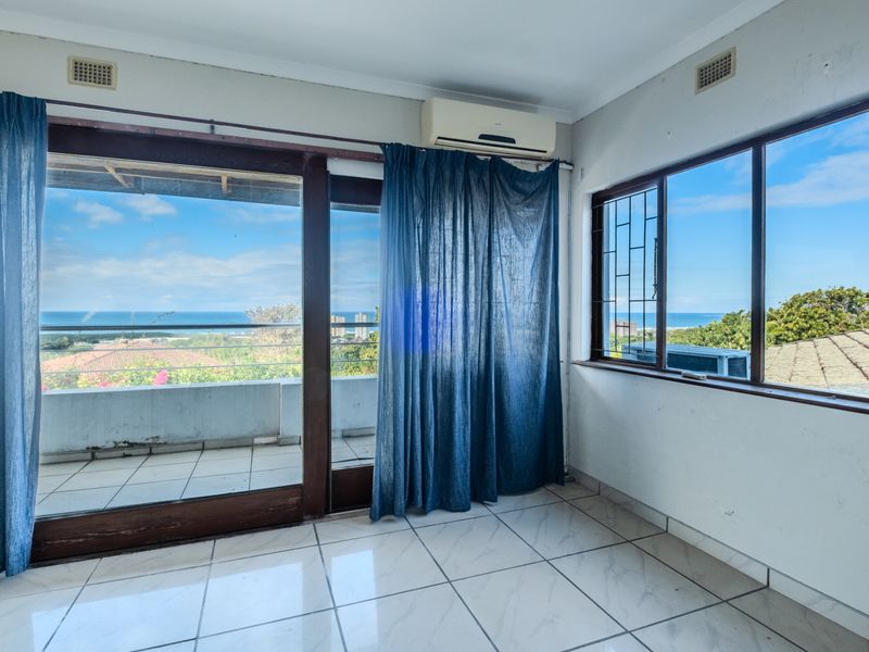 Bright living area featuring tiled floors, an air conditioning unit, and large sliding doors opening to a balcony with scenic ocean views.