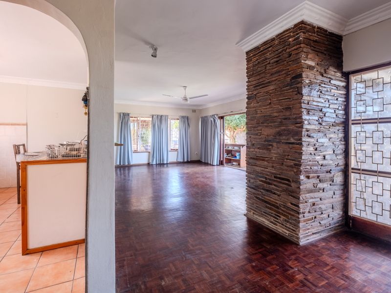 Spacious open-plan living area featuring parquet flooring, a striking stone-clad feature pillar, and an arched transition to the adjacent kitchen space.