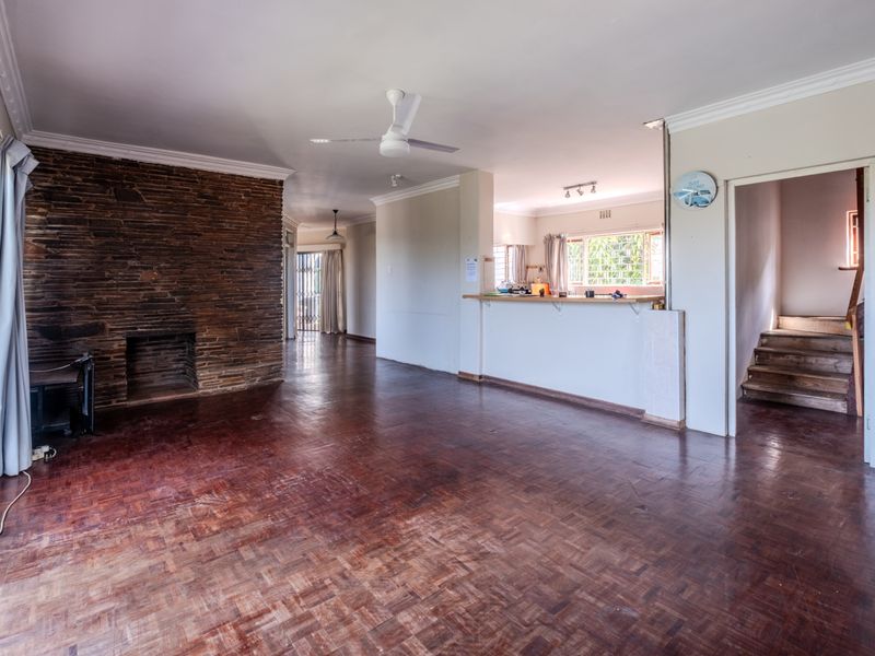 Spacious open-plan living area featuring parquet flooring, a prominent stone fireplace, and a breakfast bar connecting to the kitchen space.