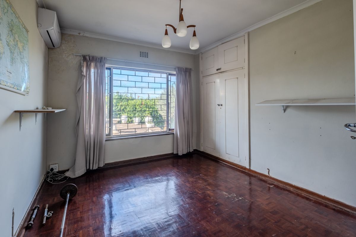 A vacant bedroom featuring original parquet flooring, built-in cupboards, and an air conditioning unit, requiring cosmetic updates to the wall finishes.