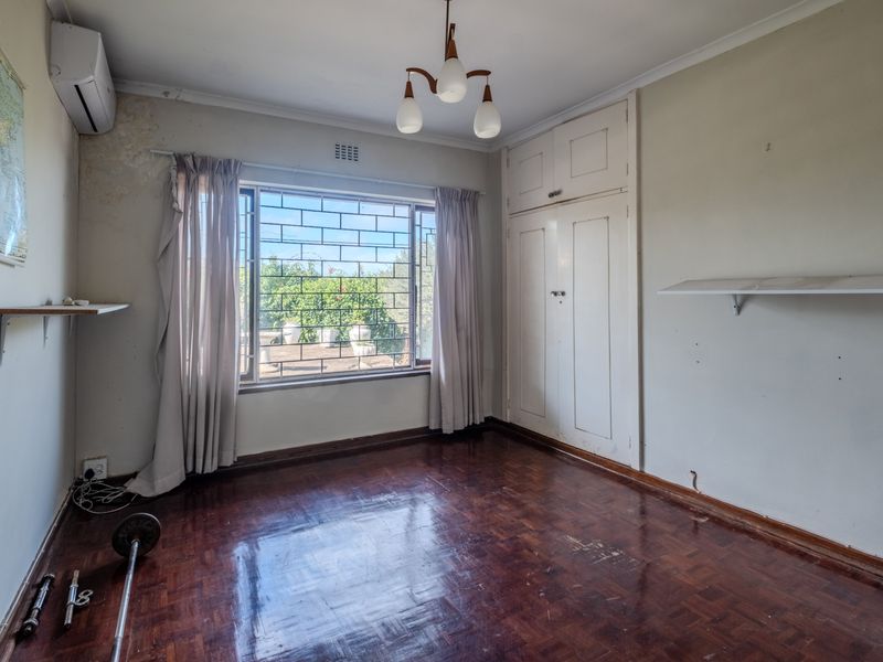 A vacant bedroom featuring original parquet flooring, built-in cupboards, and an air conditioning unit, requiring cosmetic updates to the wall finishes.