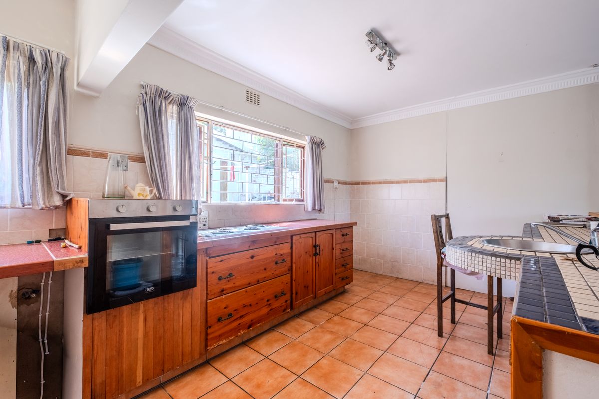 A dated kitchen featuring wooden cabinetry, tiled countertops, and a built-in oven, offering a functional layout with potential for modern renovation.