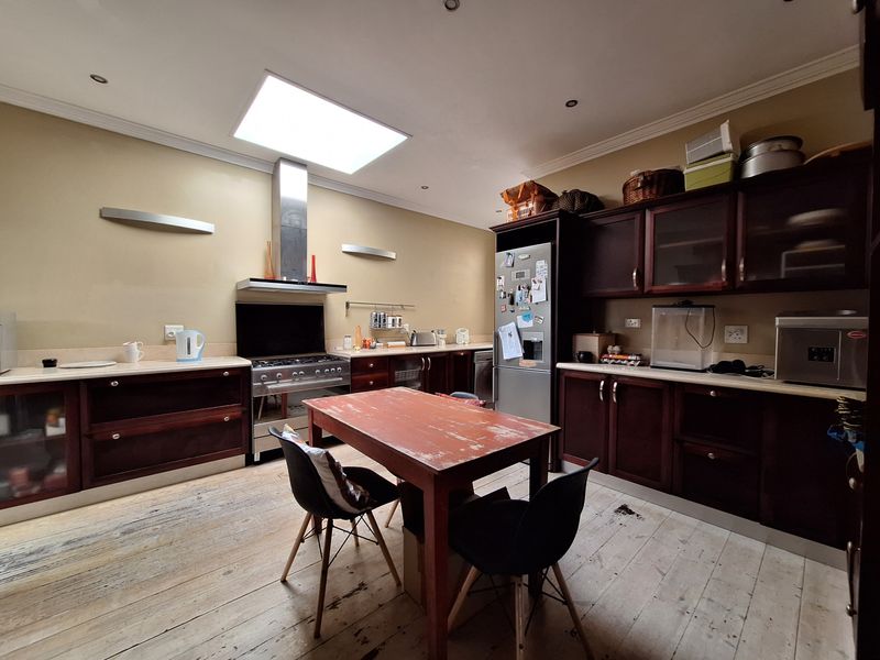 Spacious kitchen featuring dark wood cabinetry, a gas stove with stainless steel extractor, and a large skylight, set over rustic timber flooring.