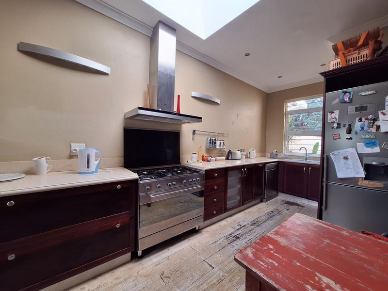 A kitchen featuring dark wood cabinetry, stone countertops, a stainless steel gas stove with extractor fan, and a skylight, with worn flooring in need of attention.
